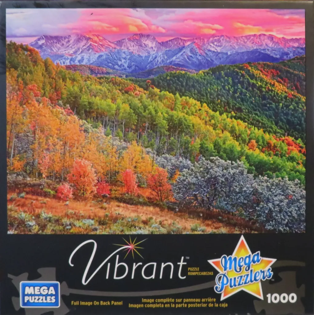 A panoramic landscape of mountain peaks glowing in sunset light above a forest with autumn foliage.