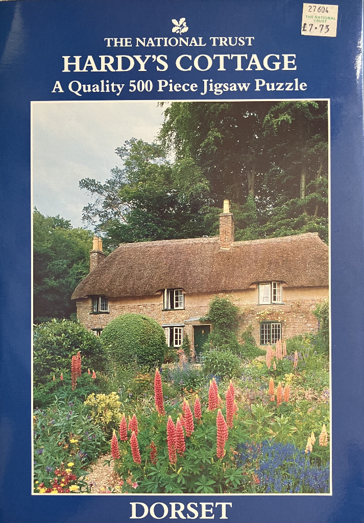 Hardy’s Cottage in Dorset with a lush foreground garden of colorful lupines and greenery.