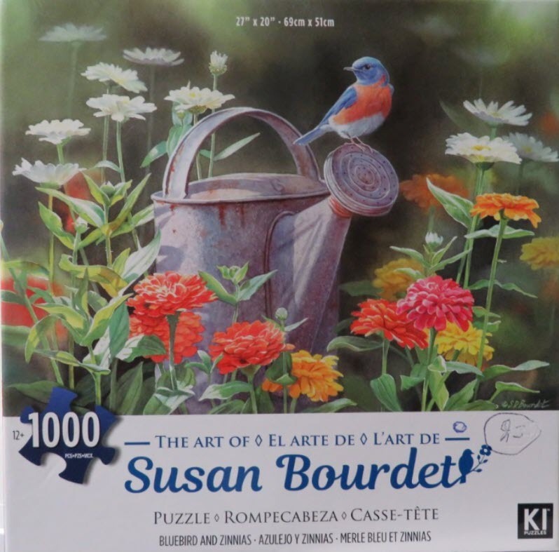 A bluebird perches on an old metal watering can surrounded by bright zinnias and daisies.