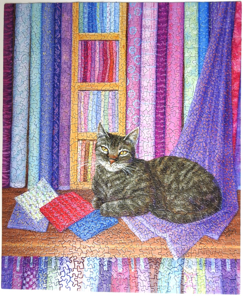 A tabby cat resting on a wooden surface in front of colorful vertical fabric bolts