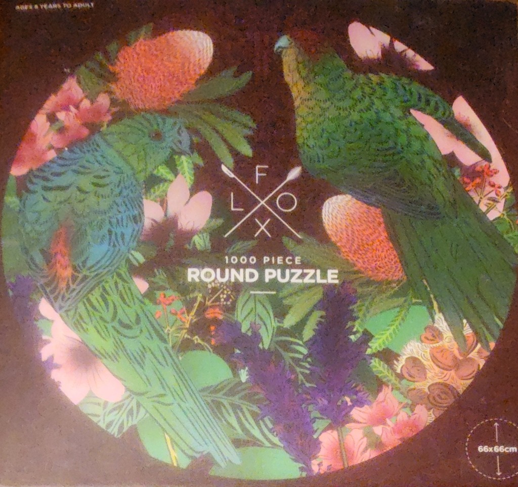 Two vibrant green parrots perched amongst native Australian flowers and foliage against a dark brown circular background.
