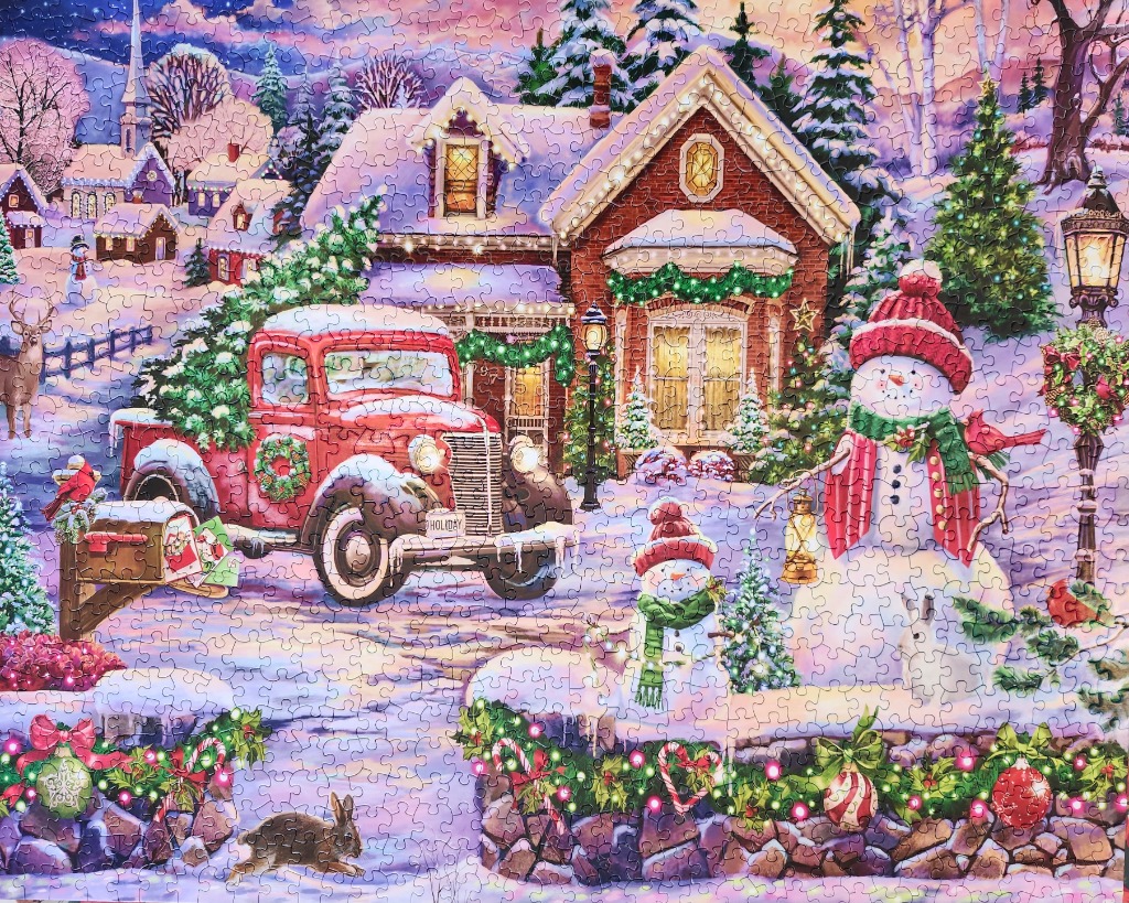 A cozy winter scene featuring a red vintage truck, snowmen, and a brick cottage decorated for Christmas.