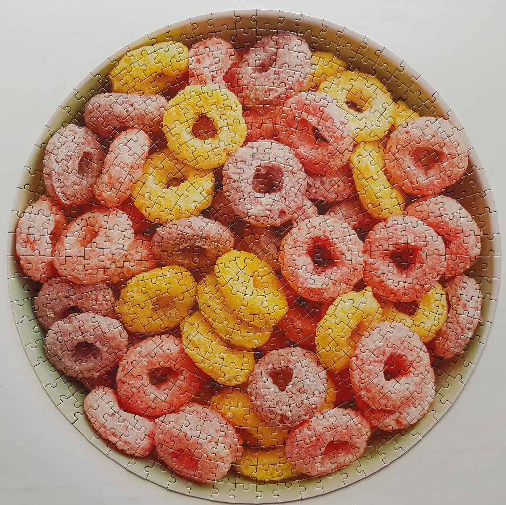 A top-down view of a round bowl filled with a mixture of bright yellow and red-dusted ring-shaped cereal.