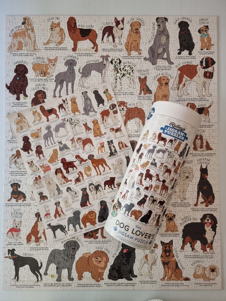 An arrangement of a dog-themed puzzle, a miniature reference print, and a cylindrical storage container.