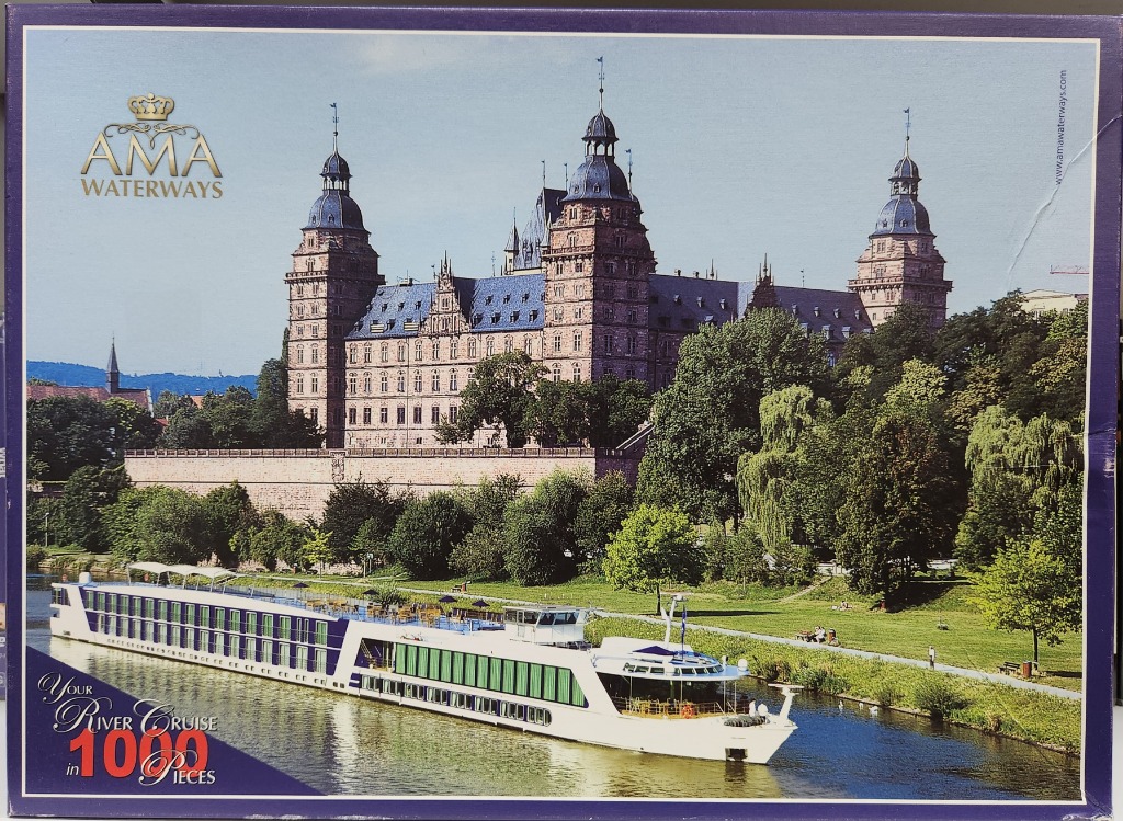 A modern white cruise ship sailing on a river in front of a grand, historic Renaissance-style castle.
