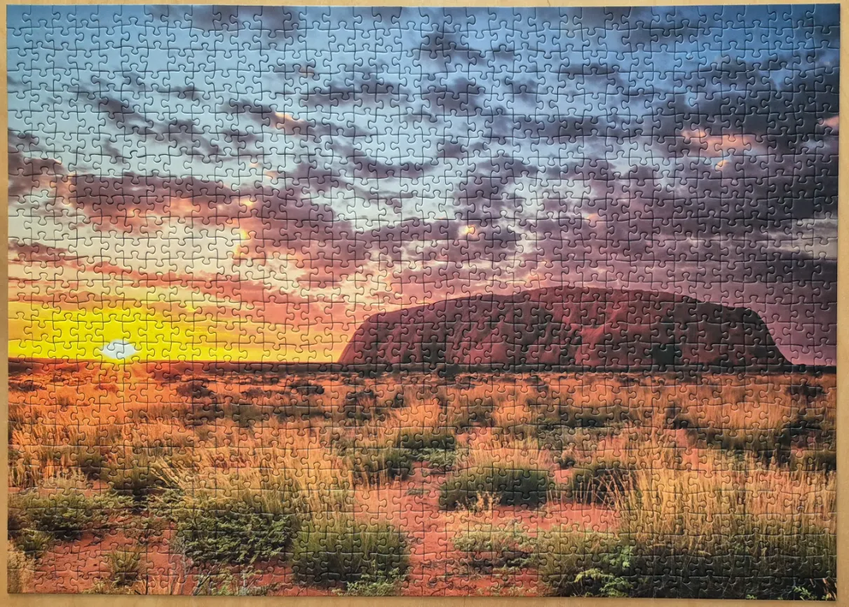 Uluru at sunset over the Australian outback with a vibrant yellow sun and orange clouds.