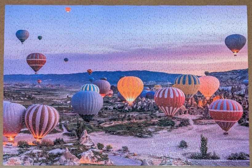 Dozens of colorful hot air balloons floating over a rugged, rocky landscape at sunrise.