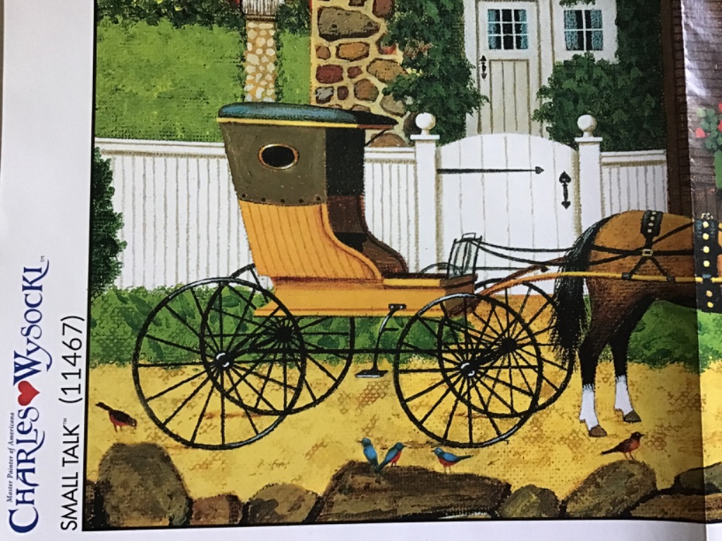 A horse-drawn carriage sits on a gravel path in front of a white picket fence and a stone house.