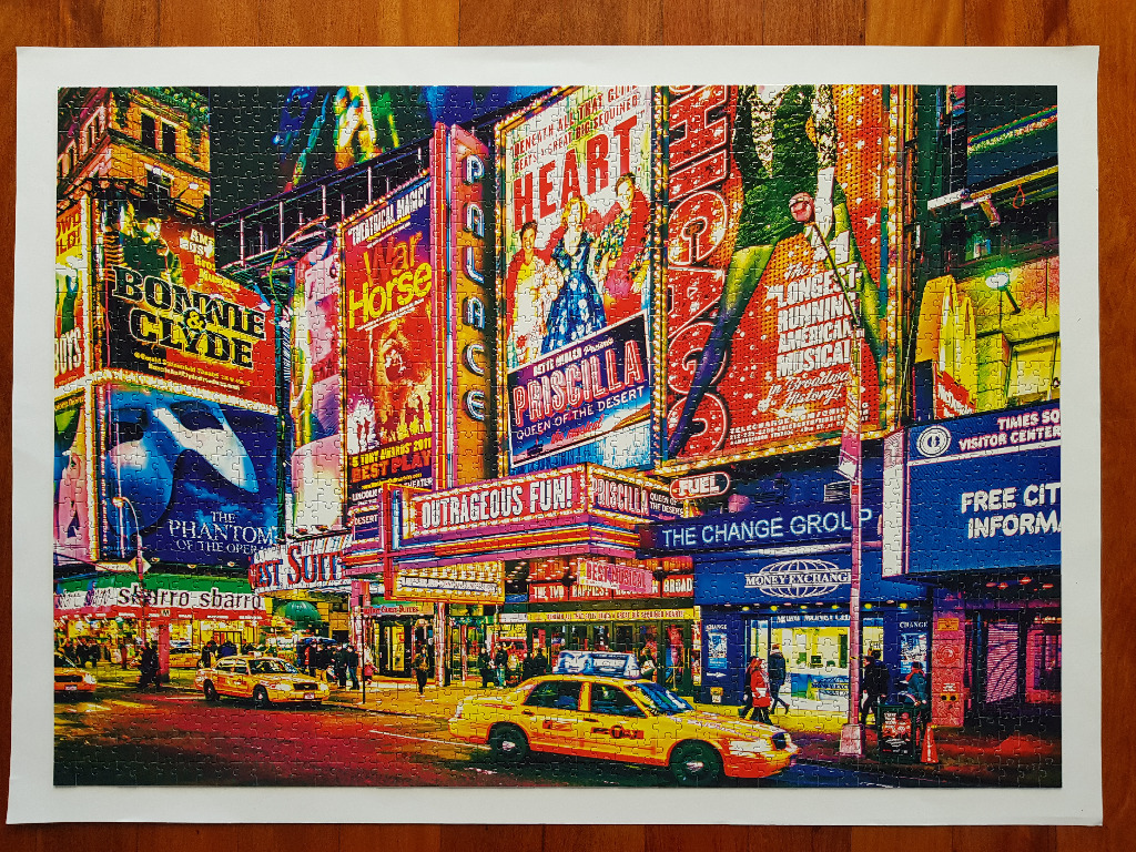A night scene of New York City's Times Square with brightly lit Broadway theatre marquees and yellow taxis.
