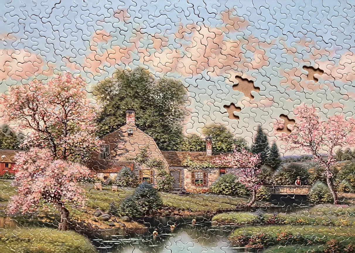 A peaceful country cottage surrounded by blooming cherry blossoms by a stream at sunset.