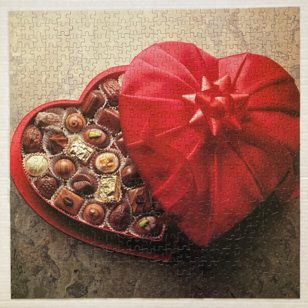 A heart-shaped box of assorted chocolates with the lid partially open on a textured grey background.