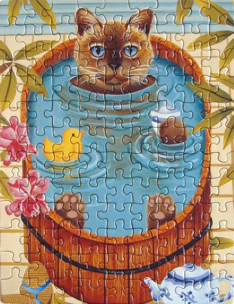 A Siamese cat with bright blue eyes sits inside a wooden tub filled with water and a yellow rubber duck.