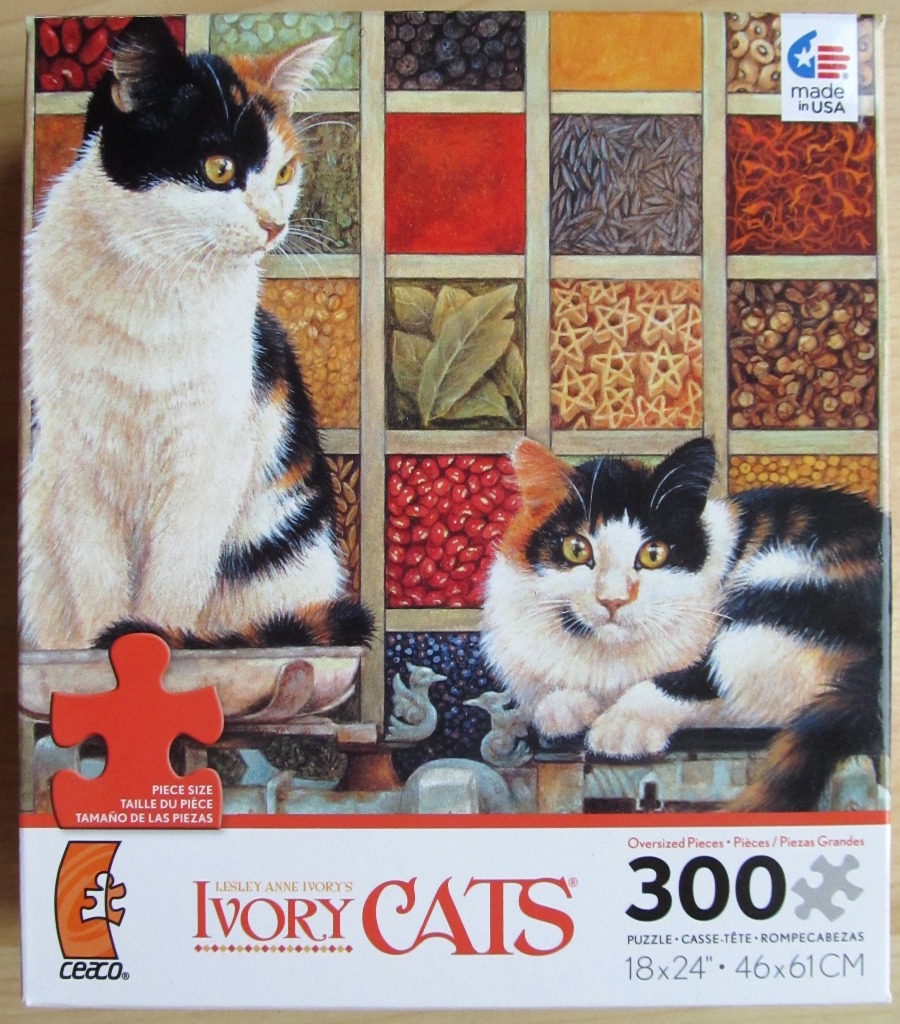 Two calico cats posing in front of a grid of containers filled with various grains, spices, and pasta shapes.