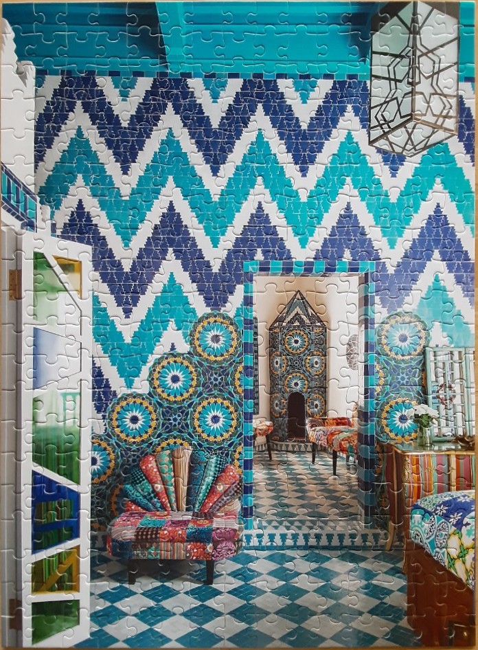 A vibrantly decorated room featuring blue and turquoise zig-zag tiled walls and a patchwork fan-shaped chair.