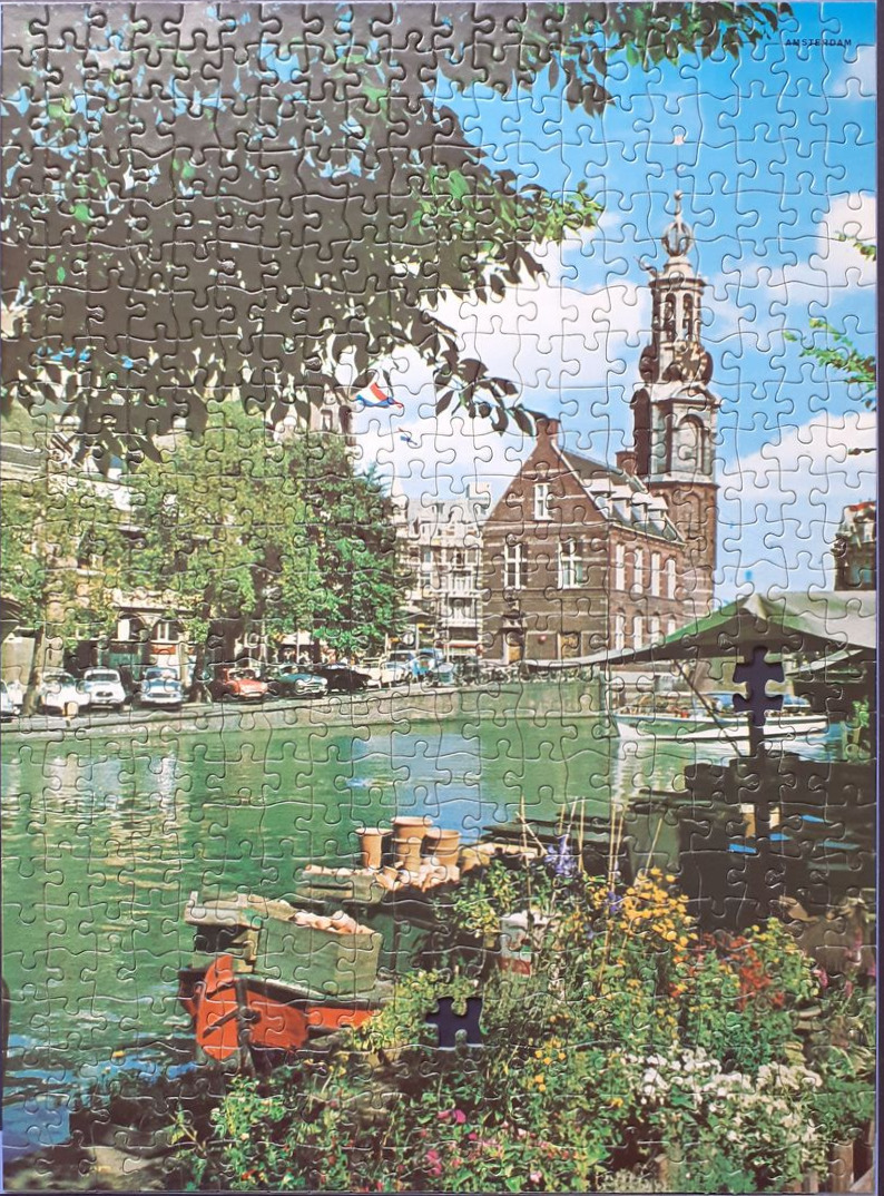 A vintage photograph showing a canal scene in Amsterdam with the Westerkerk church tower in the background.