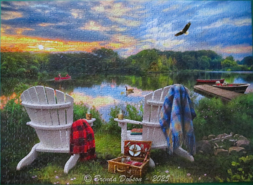 Two Adirondack chairs overlooking a lake at sunset with a picnic basket and canoes in the distance.