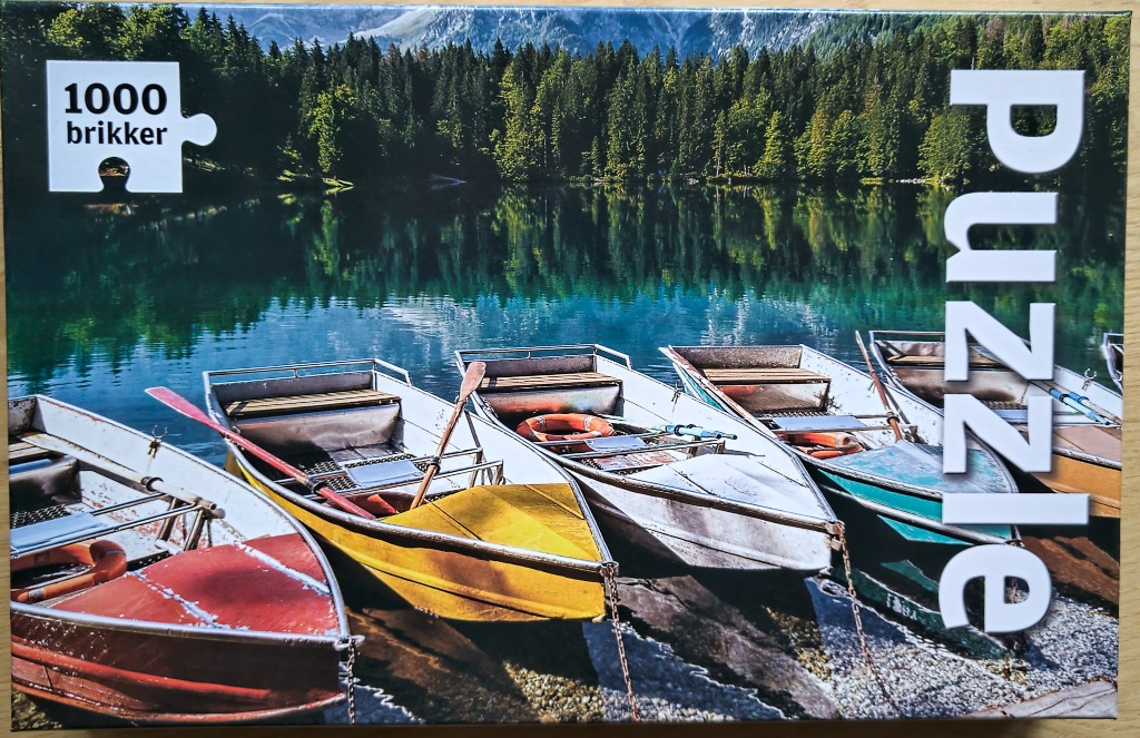 Four colorful rowboats moored at a calm mountain lake shore against a backdrop of deep green pine forests and mountains.