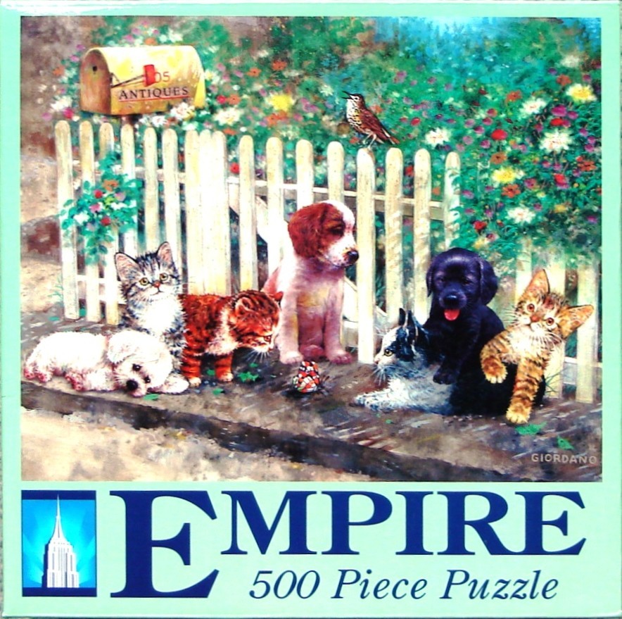 A group of puppies and kittens sitting in front of a white picket fence in a garden.