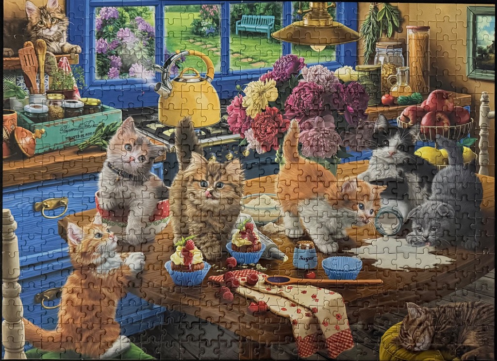 A cozy country kitchen scene populated by eight playful kittens among baking supplies, cupcakes, and flowers.