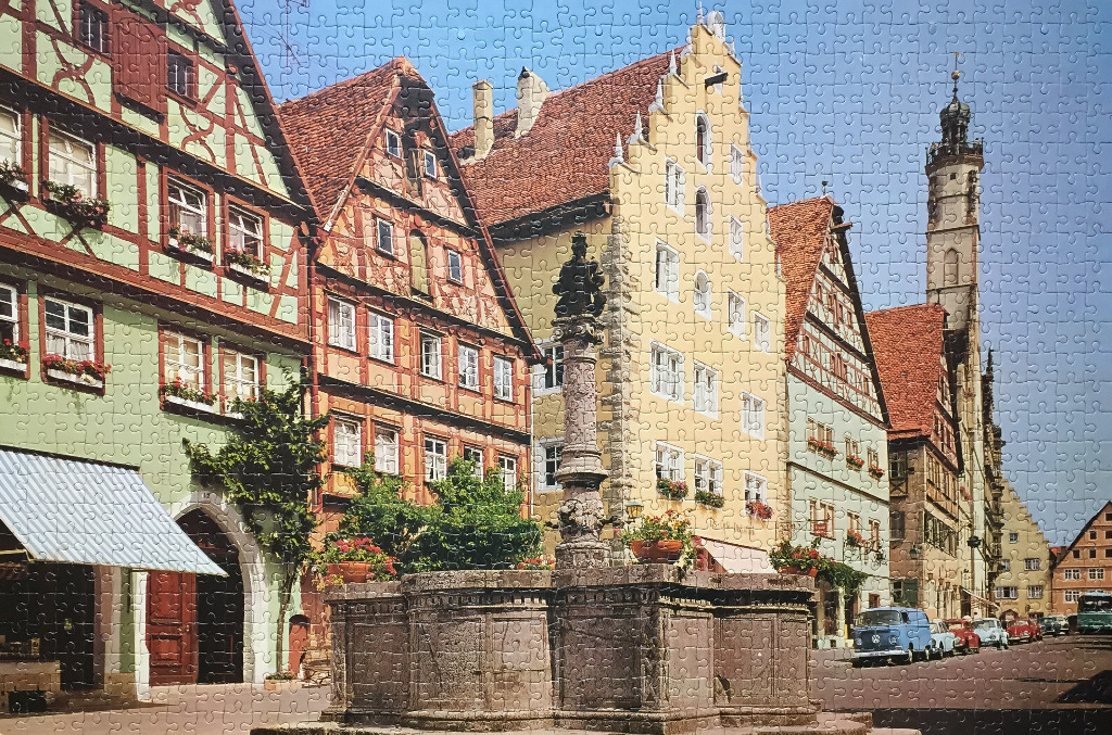 Historic German town square with colorful timbered buildings and a stone fountain under a clear blue sky.