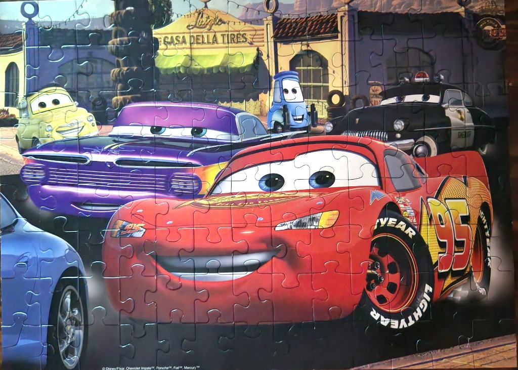 A group of animated anthropomorphic race cars gathered in front of a shop named Casa Della Tires.