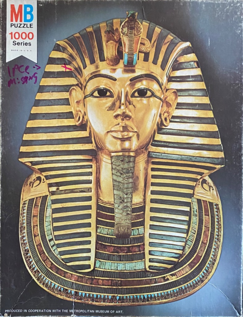 A close-up studio photograph of the golden death mask of Tutankhamun on a dark background.