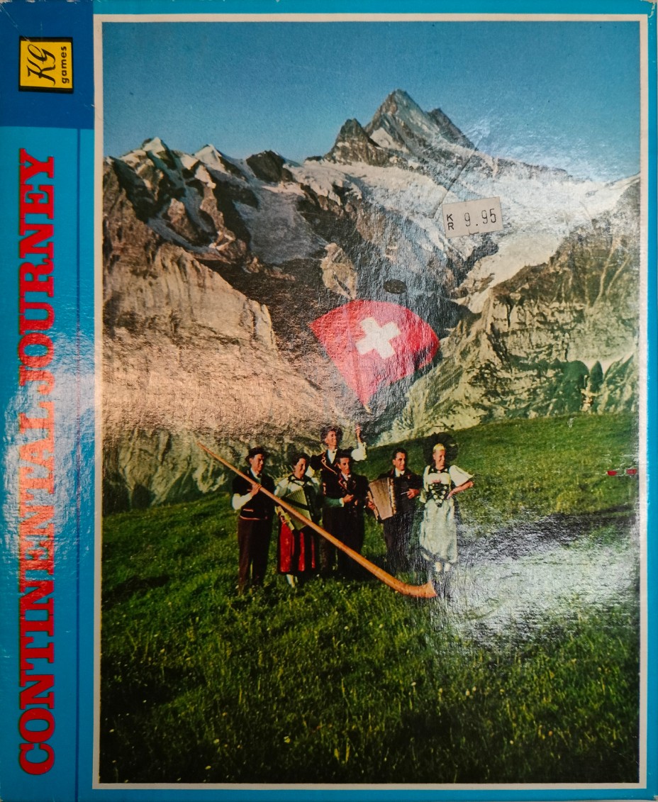 A group of musicians in traditional Swiss attire standing in a green meadow with a large mountain range in the background.
