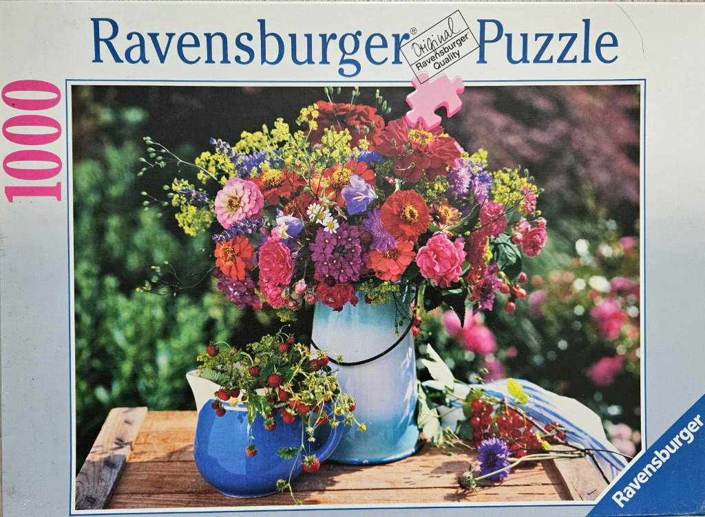A lush summer bouquet in a pale blue enamel pitcher sits on a wooden table beside a bowl of wild strawberries.