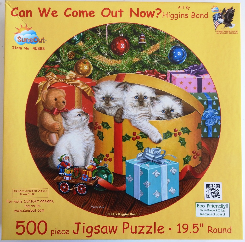 Three fluffy kittens peeking out of a decorated Christmas gift box next to a teddy bear and holiday toys.