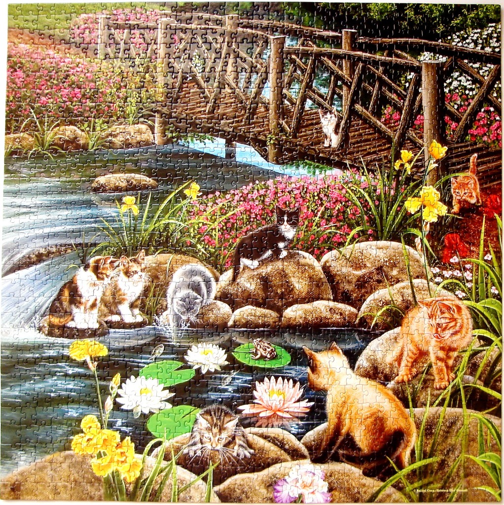 Several kittens playing near a pond and wooden bridge in a lush garden filled with flowers.