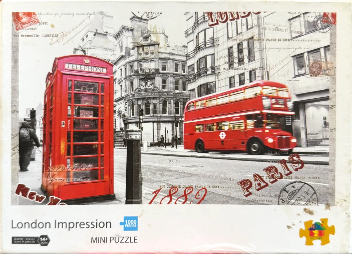 A black and white London street scene featuring a vibrant red telephone box and a red double-decker bus.