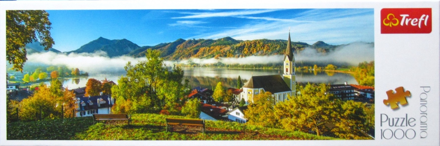Panoramic landscape of an Austrian lakeside village with a church during autumn, featuring misty mountains and fall trees.