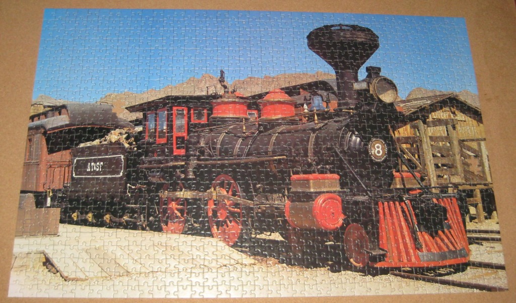 A vintage black and red steam locomotive parked at a desert station.