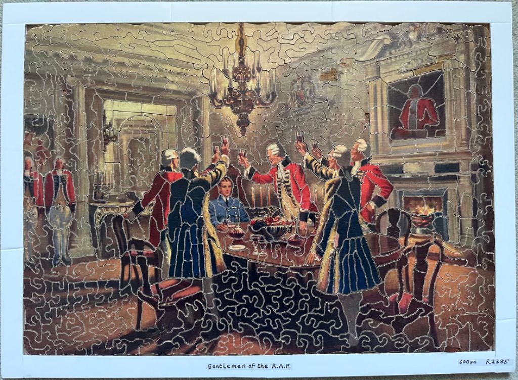 A group of 18th-century gentlemen in red coats toasting a modern RAF pilot in a candlelit room.