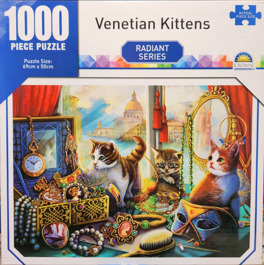 Three kittens sitting among Venetian-themed jewelry, masks, and trinkets overlooking a canal scene.