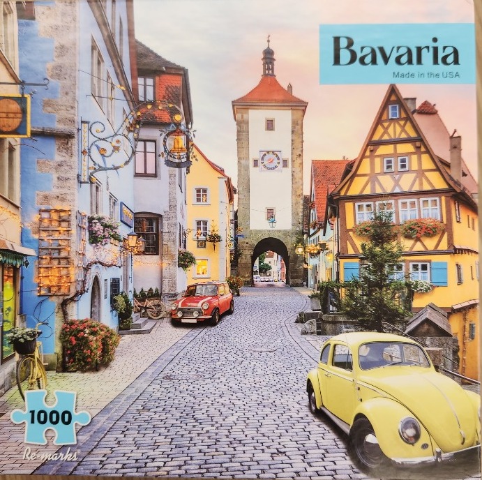 A charming European village street with a stone clock tower, half-timbered houses, and two vintage cars.