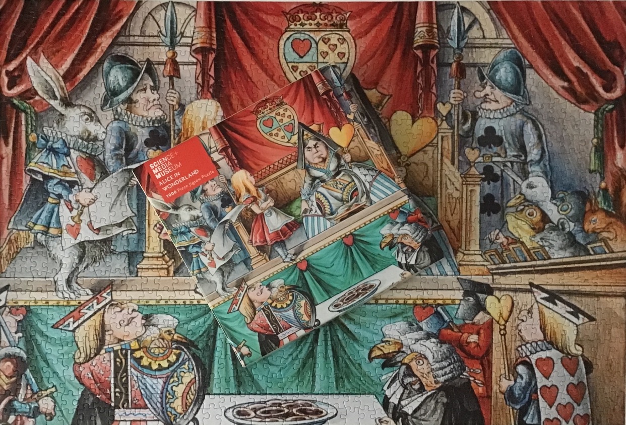 An illustration from Alice in Wonderland showing Alice standing before the Queen of Hearts in a crowded courtroom.