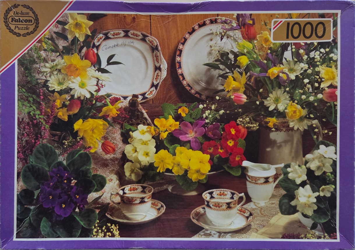 A still life featuring floral arrangements, vintage fine china, and tea cups on a wooden table.