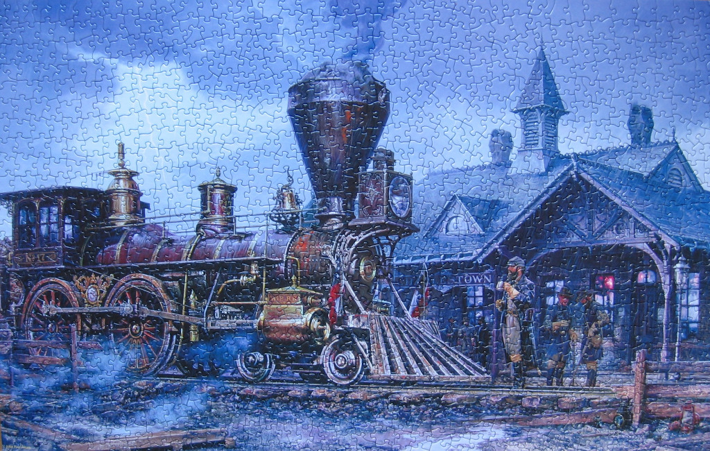 A vintage steam locomotive at a station during a foggy blue evening.