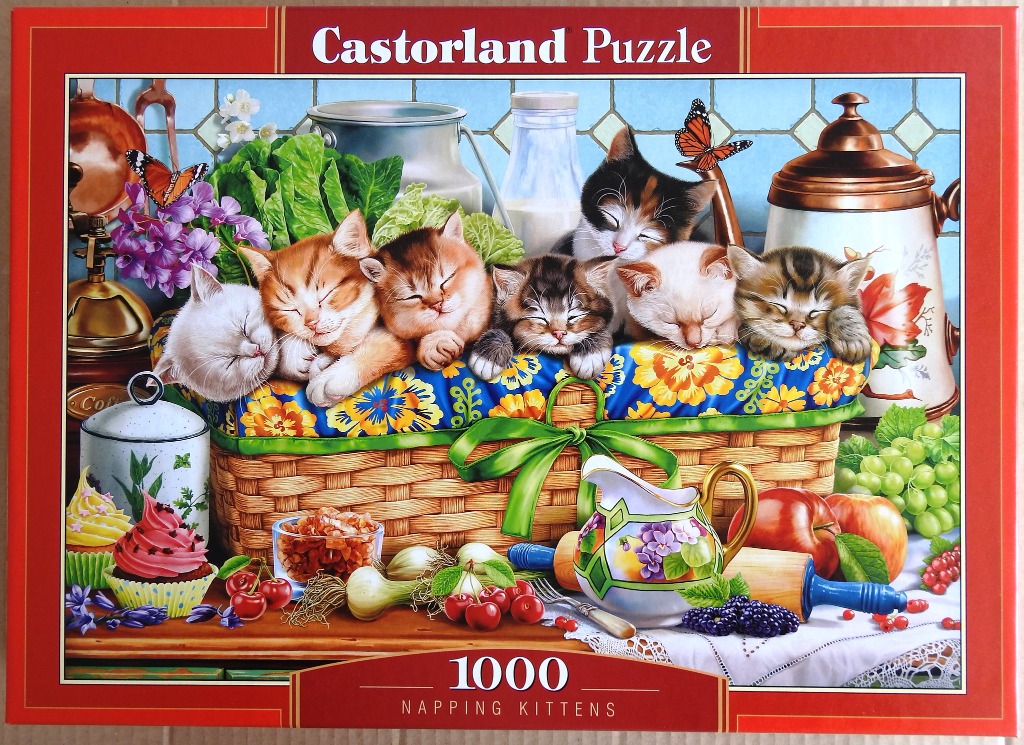 Six kittens sleeping in a wicker basket filled with colorful flowers and surrounded by kitchen items and fruit.