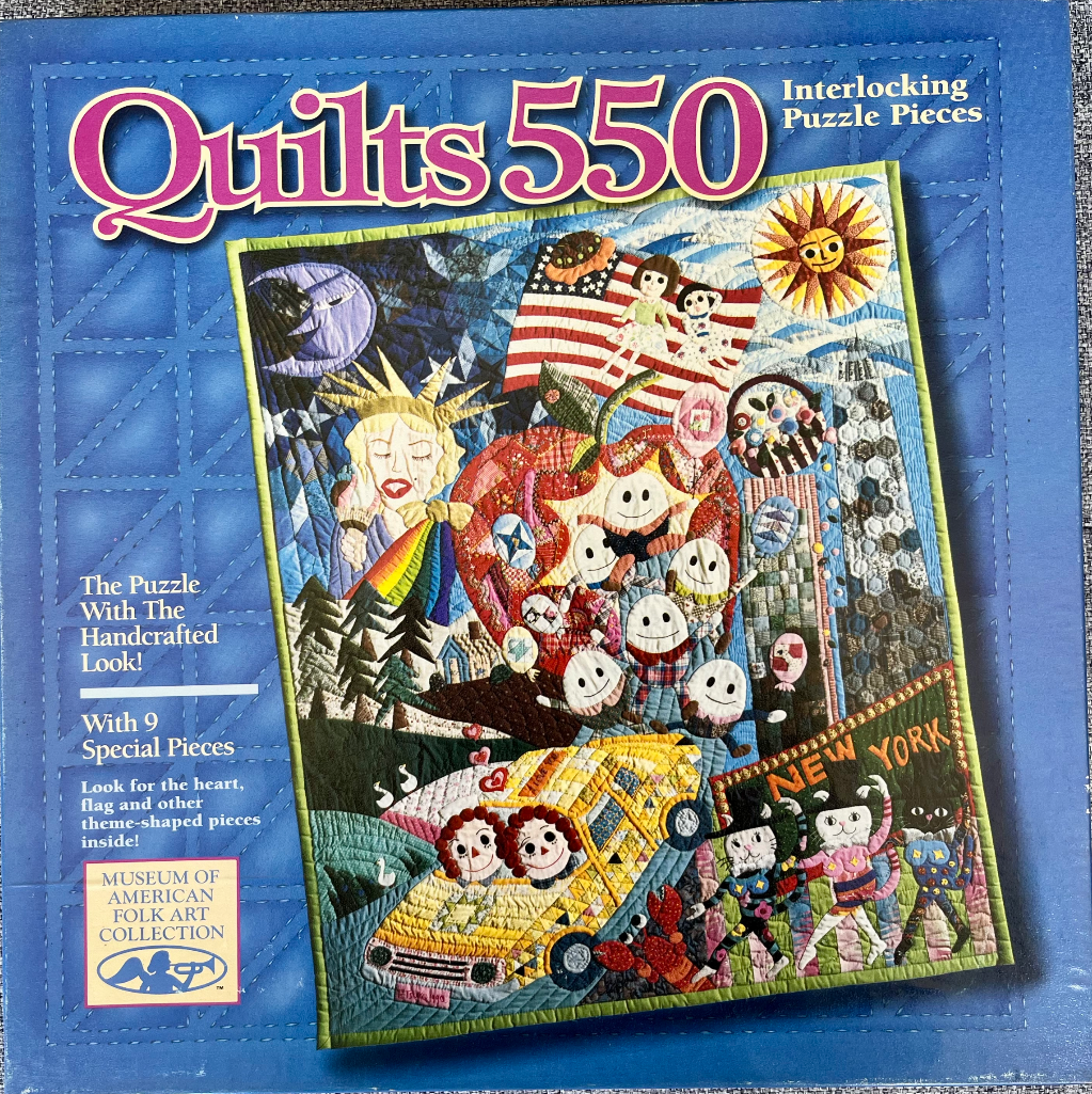 An American folk art style quilt depicting New York City scenes including the Statue of Liberty, an apple, and cats.