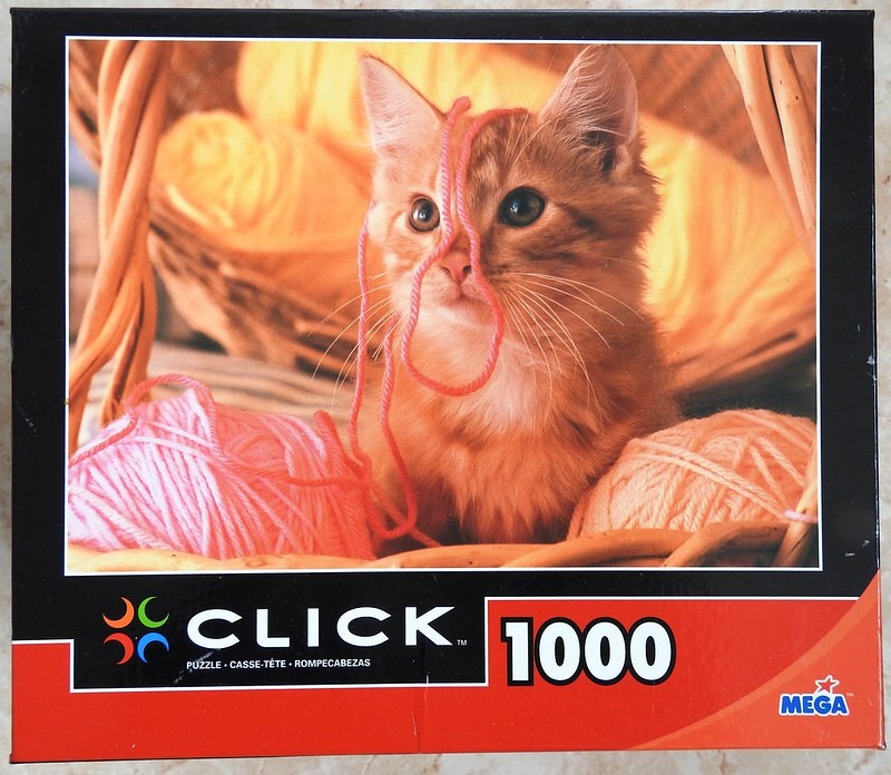 A close-up photograph of an orange tabby kitten sitting in a wicker basket surrounded by balls of yarn.