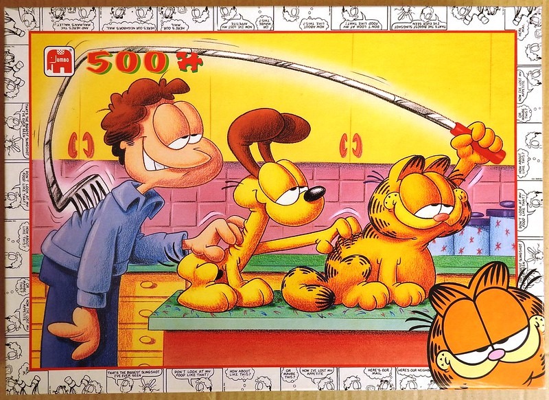 Jon Arbuckle, Odie, and Garfield in a kitchen, with Garfield using a slingshot.