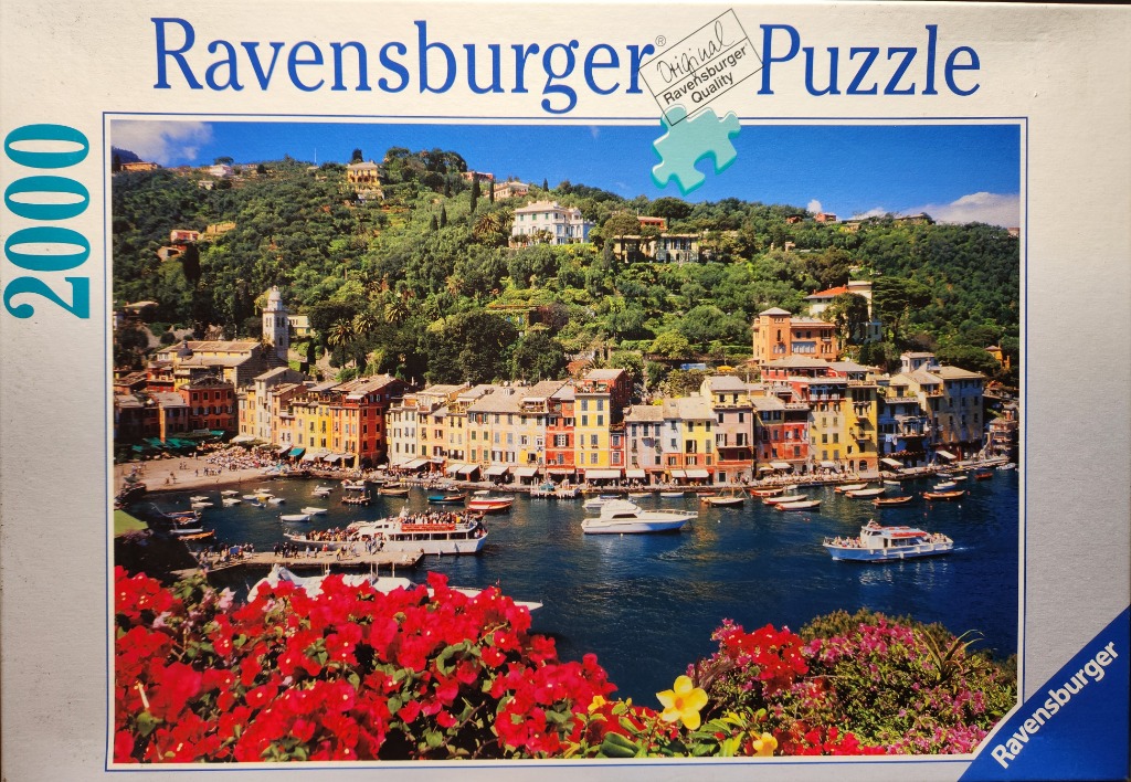 A sunny Mediterranean coastal village with colorful buildings, a harbor filled with boats, and bright bougainvillea.
