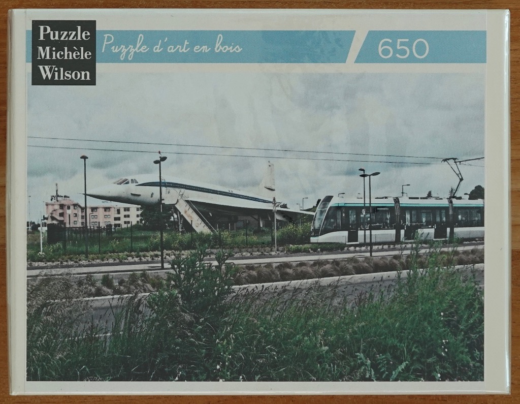 A photograph showing a retired Concorde aircraft parked next to a modern city tram on a cloudy day.
