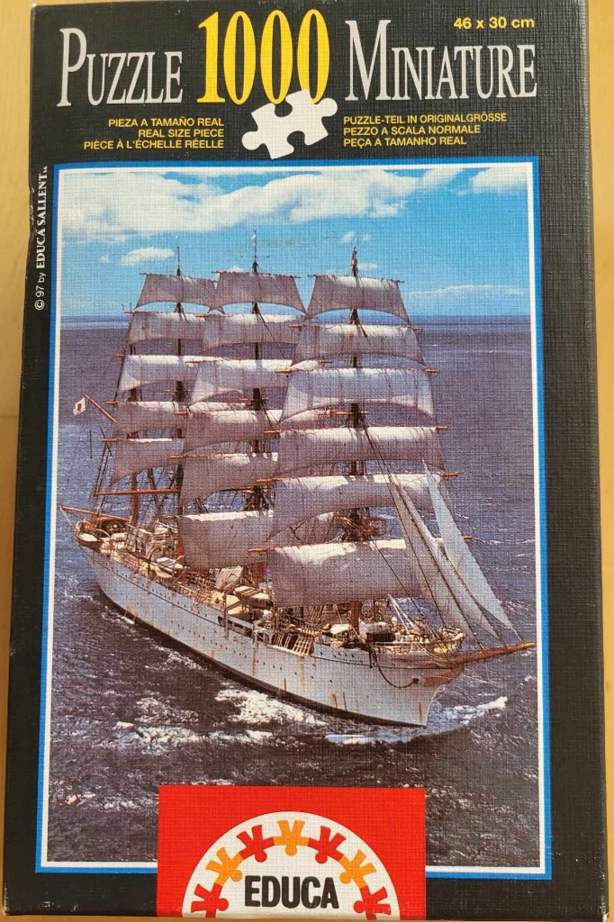A four-masted sailing ship navigating open blue water under a partly cloudy sky.