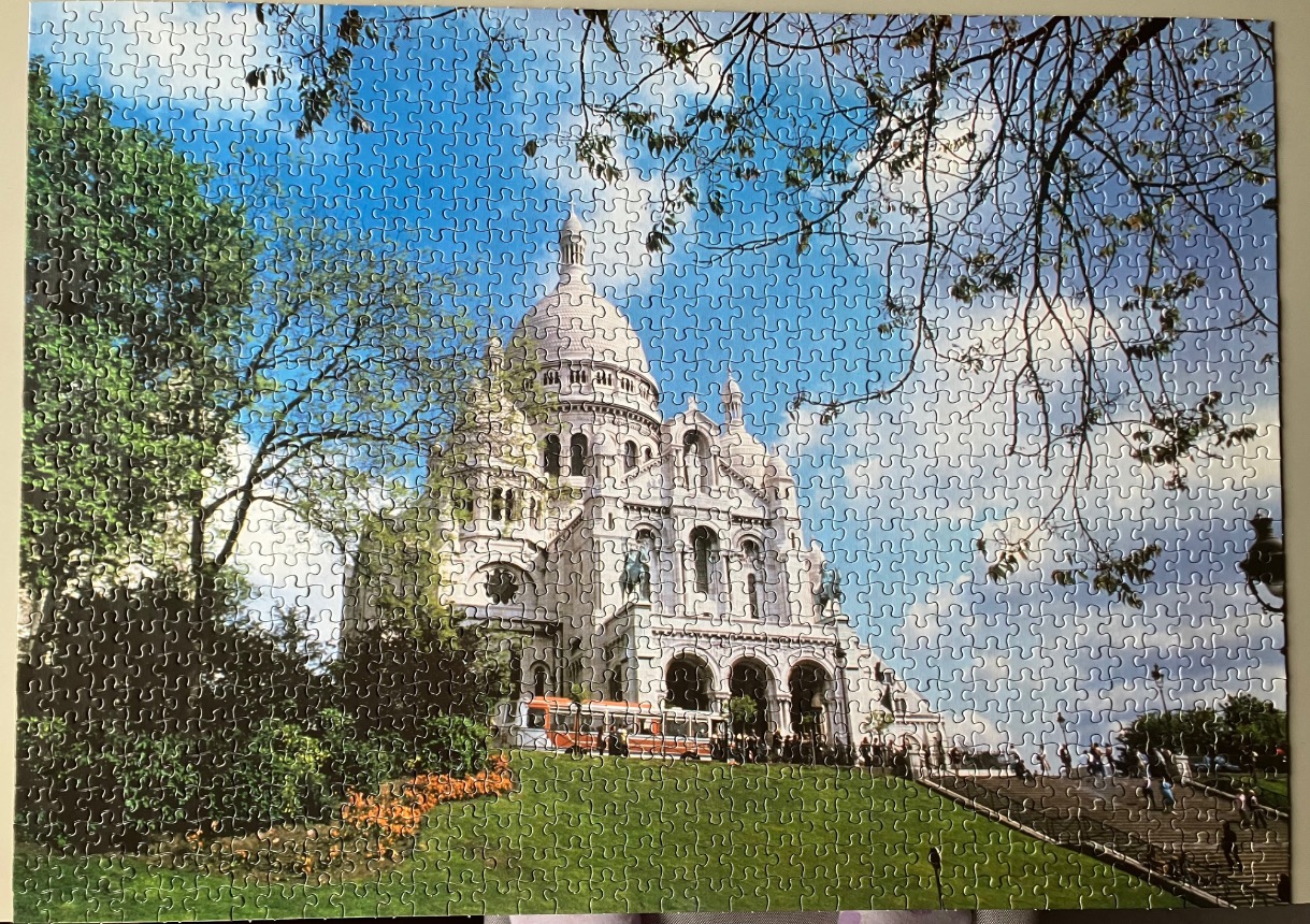 The Sacré-Cœur Basilica in Paris surrounded by lush green foliage and a clear blue sky.