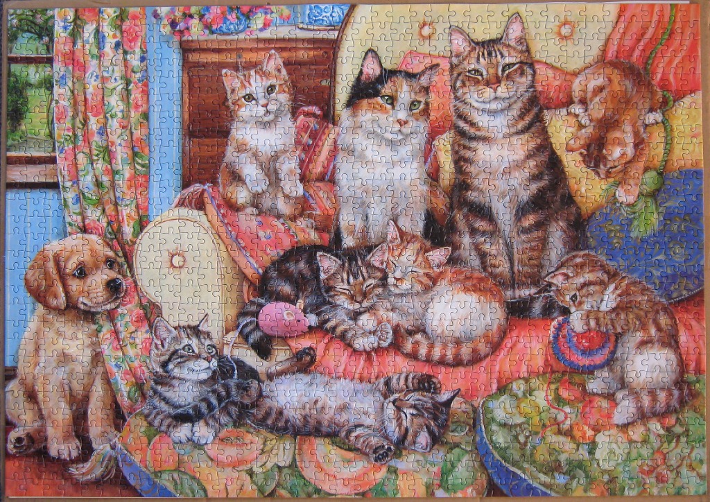 A cozy domestic scene featuring a golden retriever puppy and several cats lounging on and around a patterned sofa.