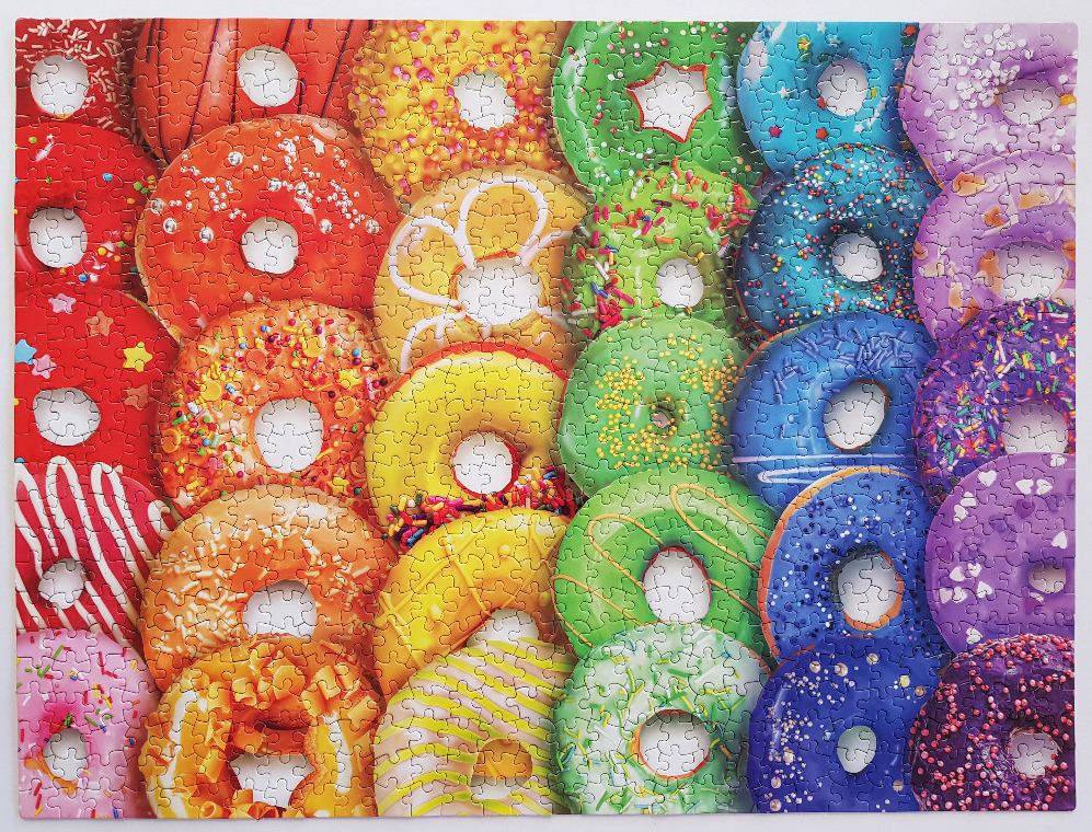 A vibrant, rainbow-colored collection of assorted glazed and sprinkled donuts arranged in a grid.