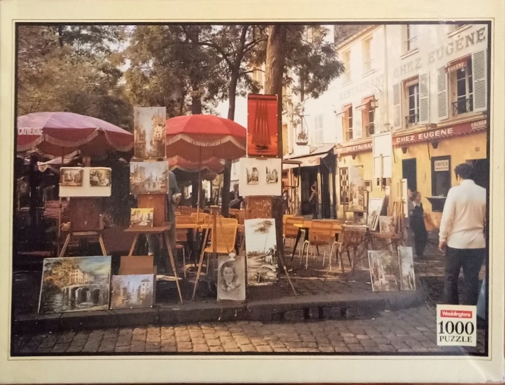 Outdoor art display at a Paris street cafe with umbrellas and paintings on easels.